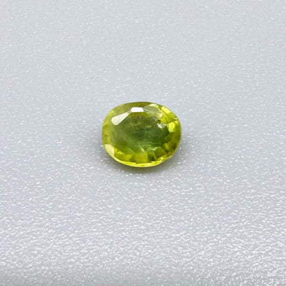 Oval greenish yellow sapphire from Thailand, 0.35ct, unheated, with bright yellow-dominant color and green undertones, visible natural inclusions and a transparent to slightly silky appearance.