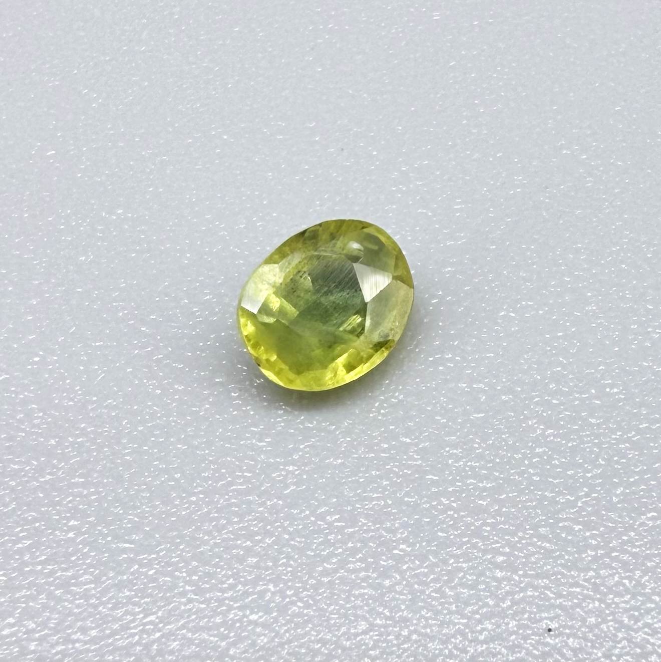 Oval greenish yellow sapphire from Thailand, 0.35ct, unheated, with bright yellow-dominant color and green undertones, visible natural inclusions and a transparent to slightly silky appearance.