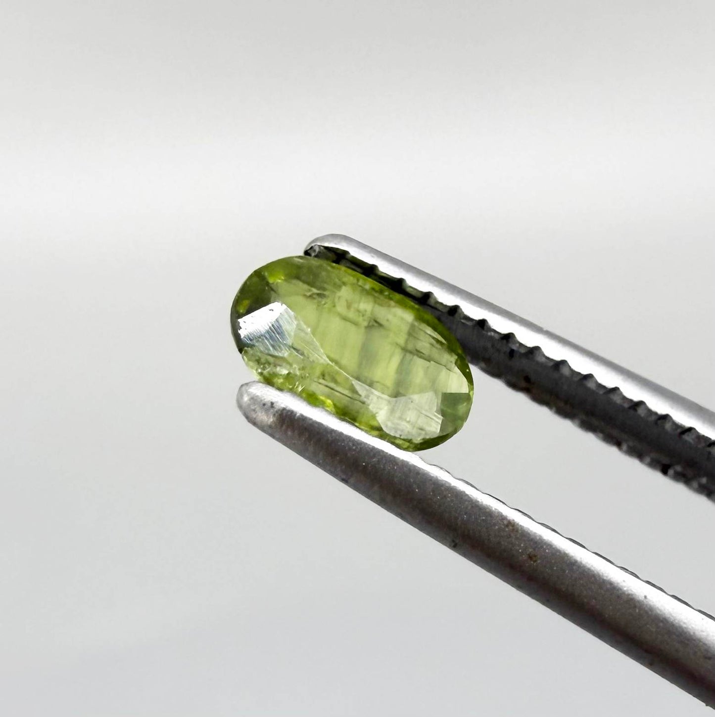 Oval green sapphire from Thailand, 0.35ct, unheated, with olive-green color, visible banding and color zoning, natural inclusions and a transparent to slightly silky appearance.