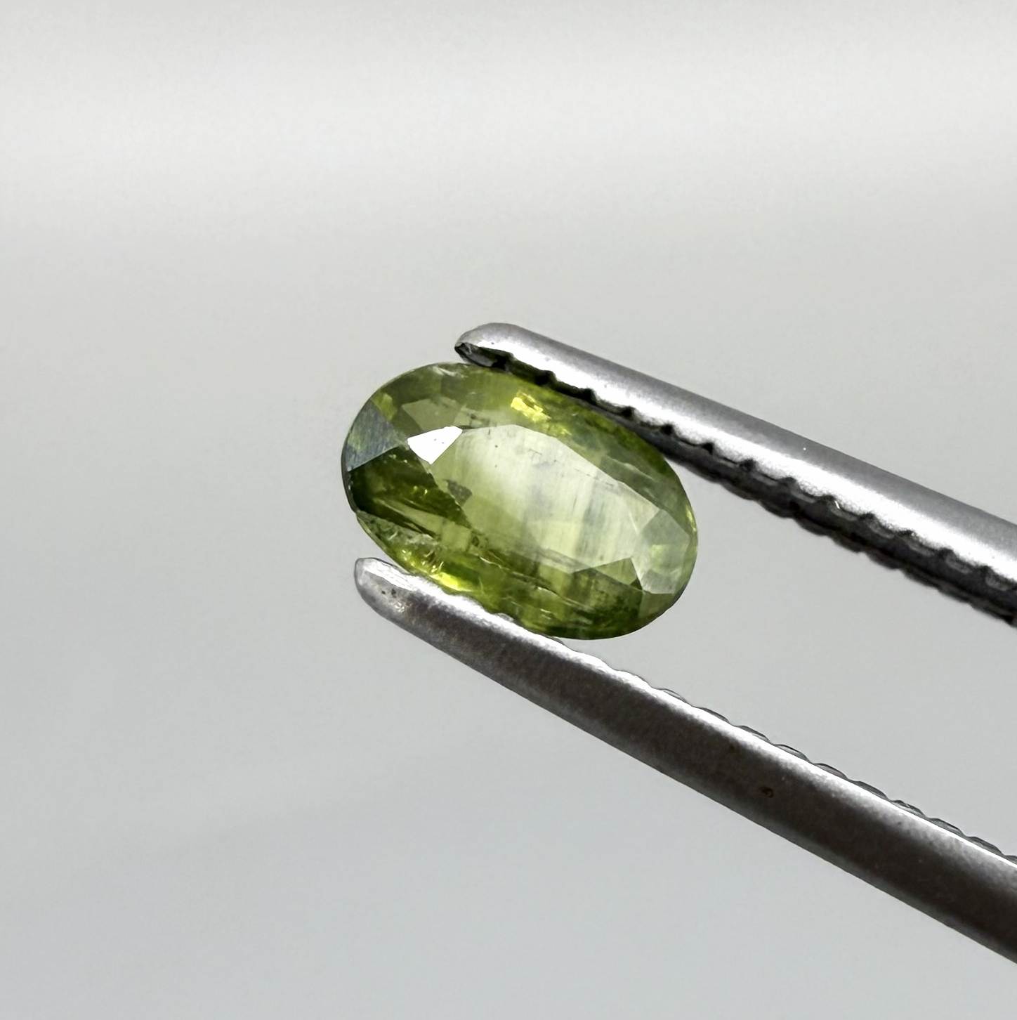 Oval green sapphire from Thailand, 0.35ct, unheated, with olive-green color, visible banding and color zoning, natural inclusions and a transparent to slightly silky appearance.