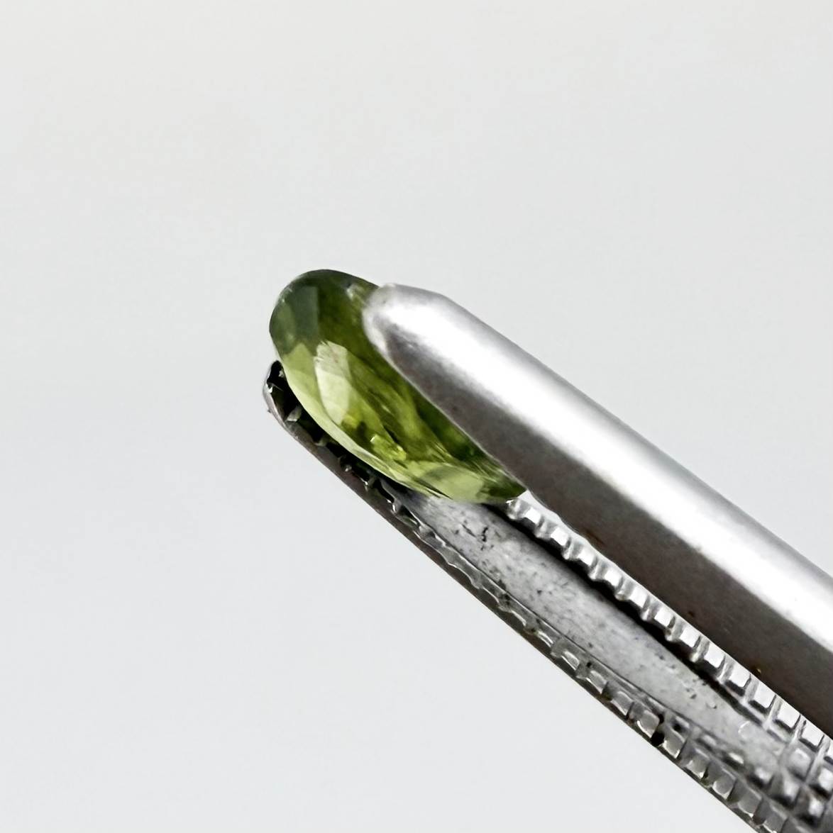 Oval green sapphire from Thailand, 0.35ct, unheated, with olive-green color, visible banding and color zoning, natural inclusions and a transparent to slightly silky appearance.