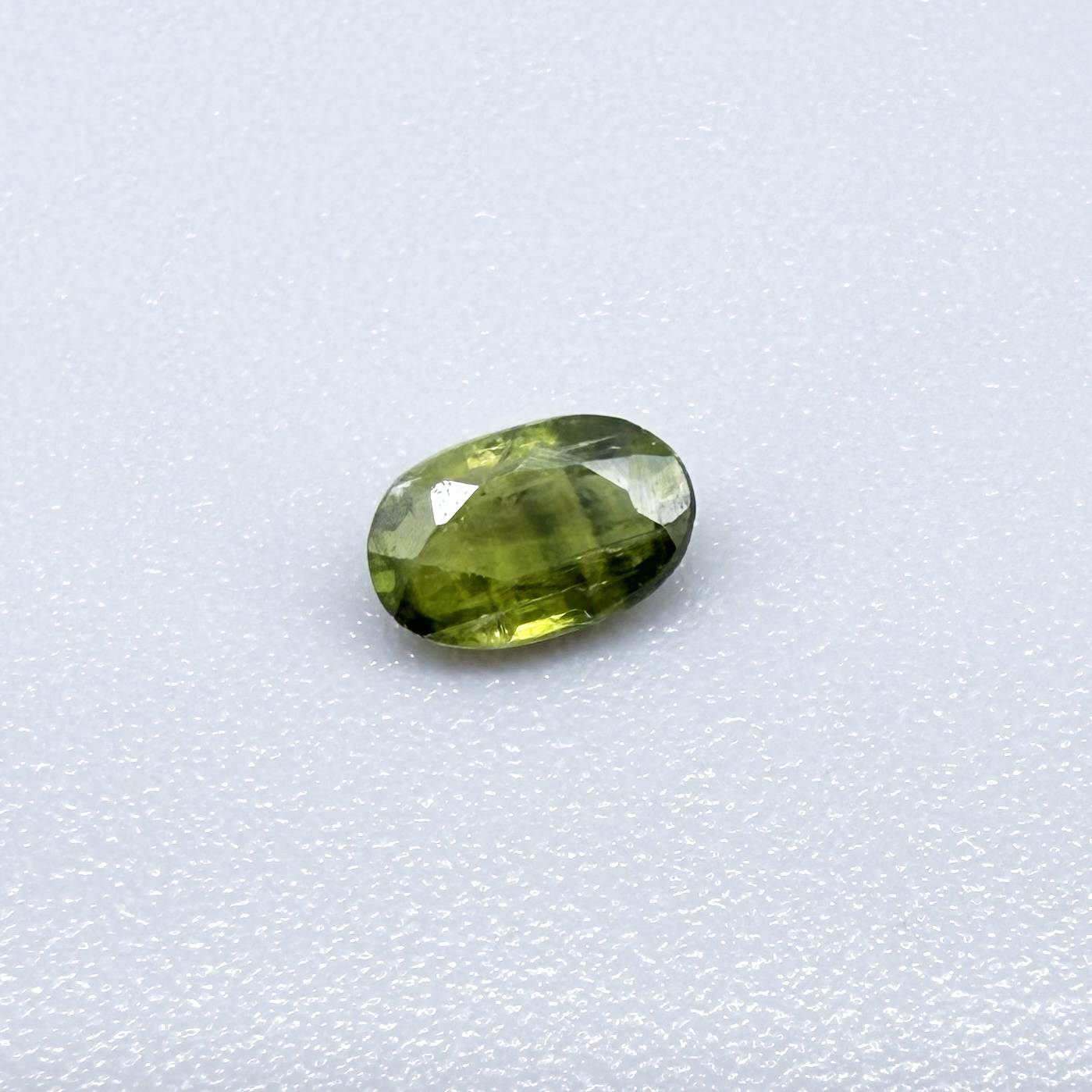Oval green sapphire from Thailand, 0.35ct, unheated, with olive-green color, visible banding and color zoning, natural inclusions and a transparent to slightly silky appearance.