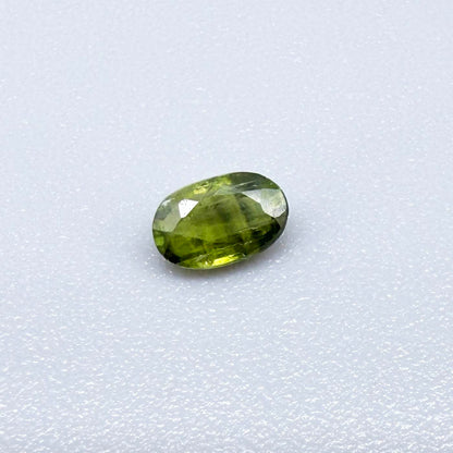 Oval green sapphire from Thailand, 0.35ct, unheated, with olive-green color, visible banding and color zoning, natural inclusions and a transparent to slightly silky appearance.