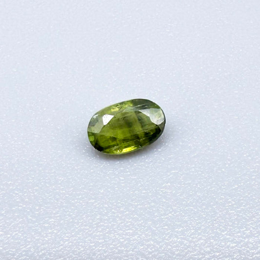 Oval green sapphire from Thailand, 0.35ct, unheated, with olive-green color, visible banding and color zoning, natural inclusions and a transparent to slightly silky appearance.