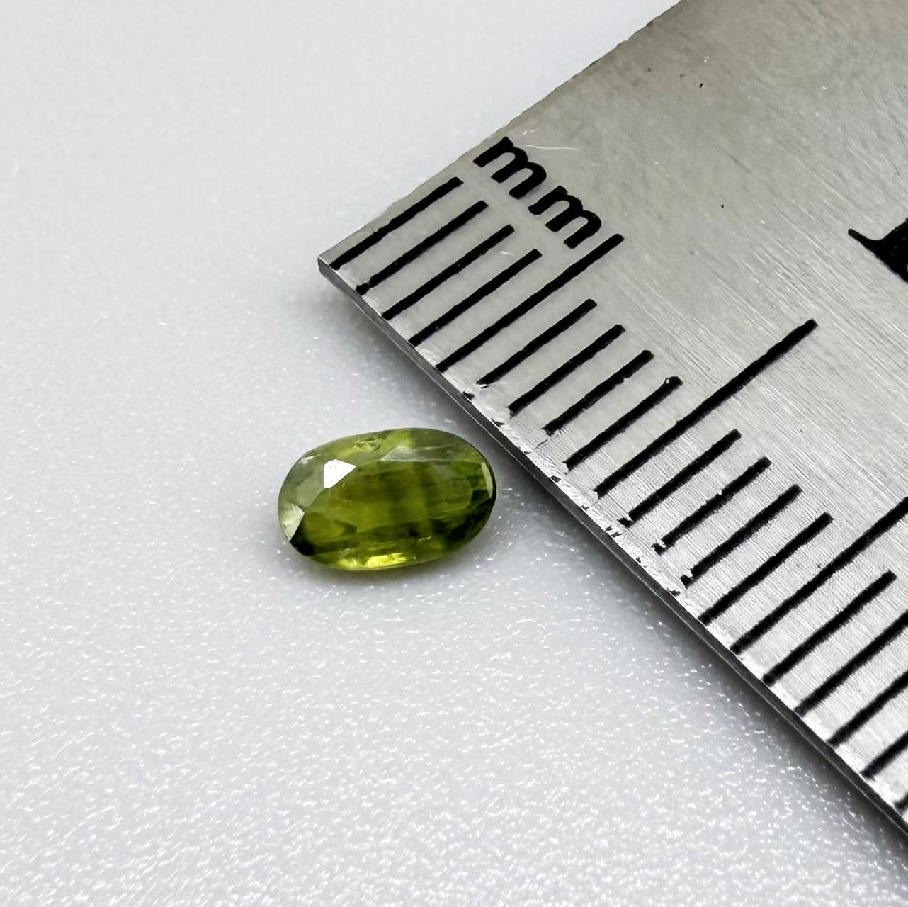 Oval green sapphire from Thailand, 0.35ct, unheated, with olive-green color, visible banding and color zoning, natural inclusions and a transparent to slightly silky appearance.