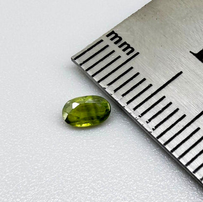 Oval green sapphire from Thailand, 0.35ct, unheated, with olive-green color, visible banding and color zoning, natural inclusions and a transparent to slightly silky appearance.
