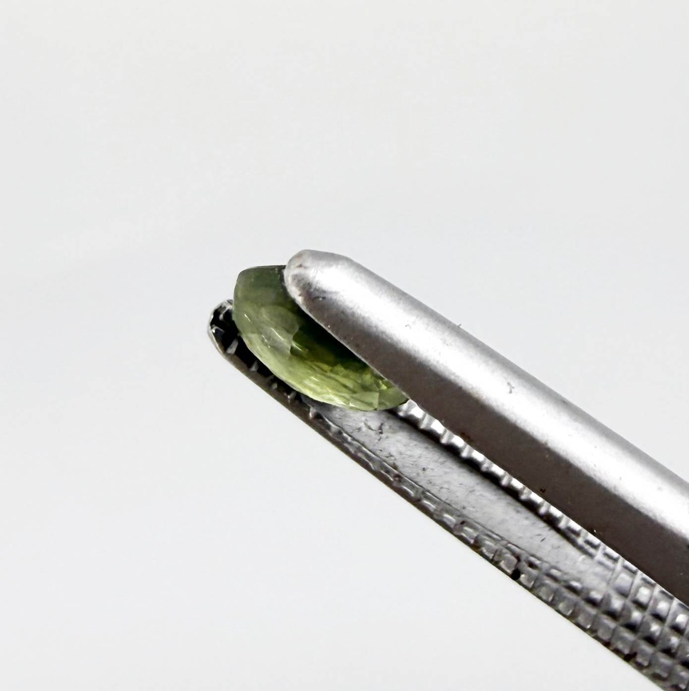 Oval green sapphire from Thailand, 0.37ct, unheated, with olive to deep green color zoning, visible natural inclusions and a transparent to slightly silky appearance.