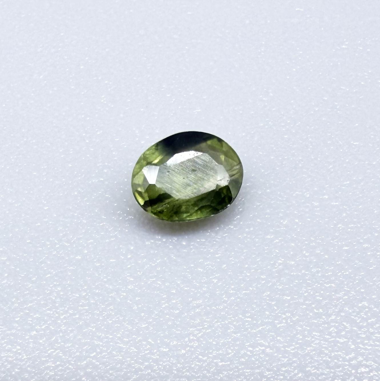 Oval green sapphire from Thailand, 0.37ct, unheated, with olive to deep green color zoning, visible natural inclusions and a transparent to slightly silky appearance.