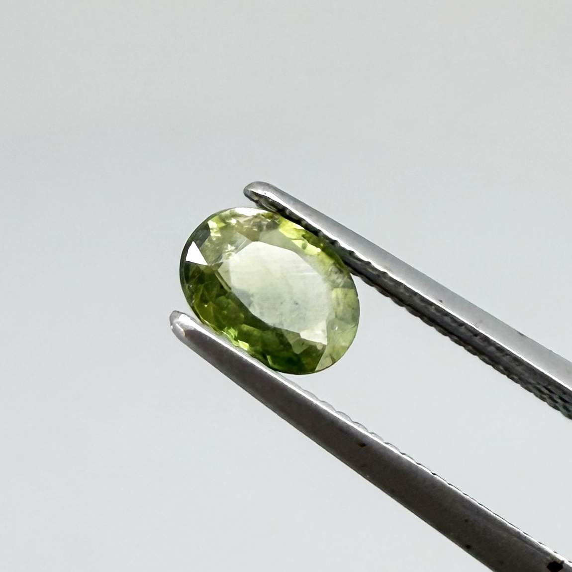Oval green sapphire from Thailand, 0.54ct, unheated, with olive-green color, visible natural inclusions and a transparent to slightly silky appearance.