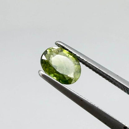 Oval green sapphire from Thailand, 0.54ct, unheated, with olive-green color, visible natural inclusions and a transparent to slightly silky appearance.