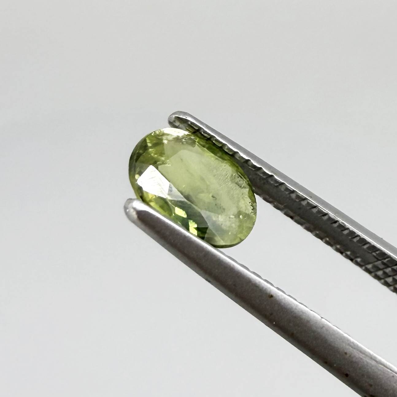 Oval green sapphire from Thailand, 0.54ct, unheated, with olive-green color, visible natural inclusions and a transparent to slightly silky appearance.