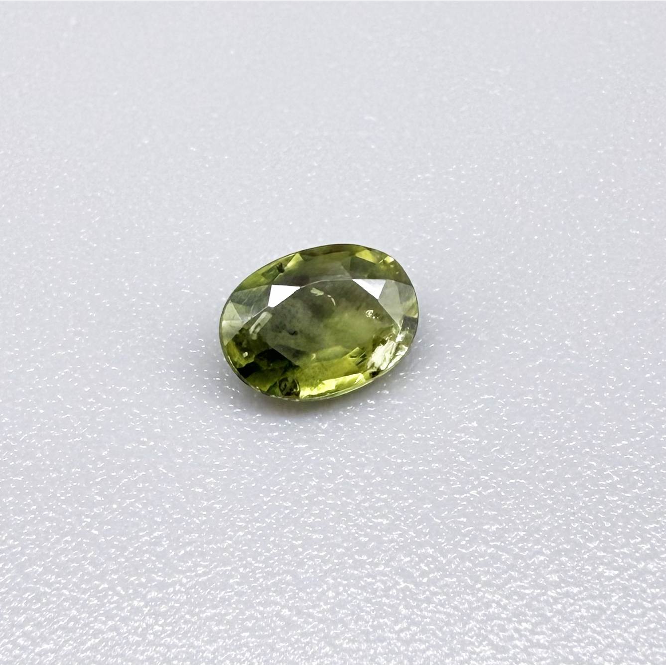 Oval green sapphire from Thailand, 0.54ct, unheated, with olive-green color, visible natural inclusions and a transparent to slightly silky appearance.