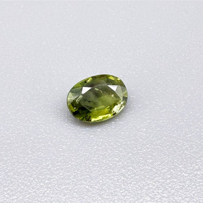 Oval green sapphire from Thailand, 0.54ct, unheated, with olive-green color, visible natural inclusions and a transparent to slightly silky appearance.