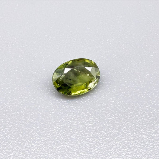 Oval green sapphire from Thailand, 0.54ct, unheated, with olive-green color, visible natural inclusions and a transparent to slightly silky appearance.