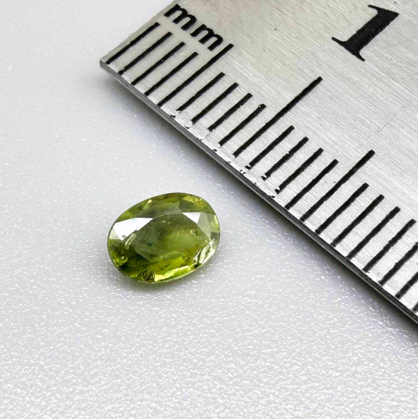 Oval green sapphire from Thailand, 0.54ct, unheated, with olive-green color, visible natural inclusions and a transparent to slightly silky appearance.