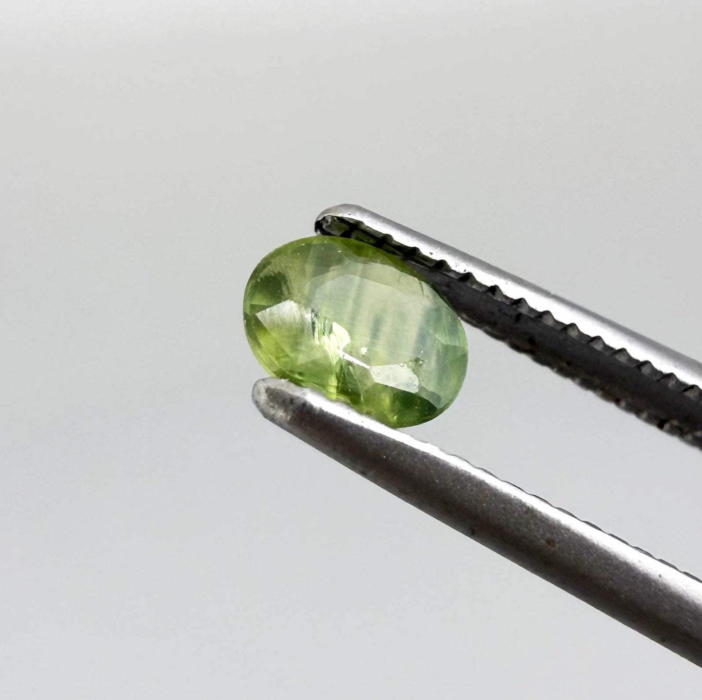 Oval light green sapphire from Thailand, 0.33ct, unheated, with soft green color, visible banding and natural inclusions and a transparent to slightly silky appearance.