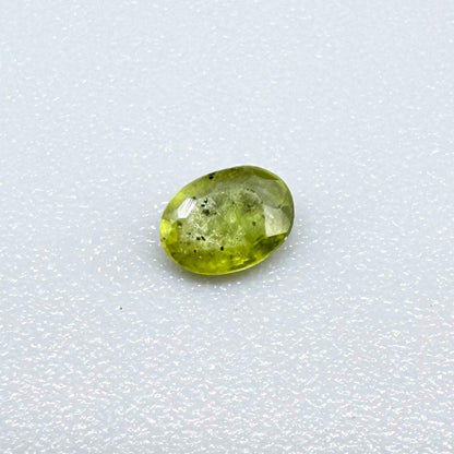 Oval yellow-green sapphire from Thailand, 0.21ct, unheated, with bright greenish-yellow color, visible dark natural inclusions and a transparent to slightly silky appearance.