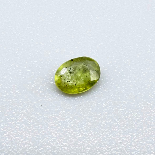 Oval yellow-green sapphire from Thailand, 0.21ct, unheated, with bright greenish-yellow color, visible dark natural inclusions and a transparent to slightly silky appearance.
