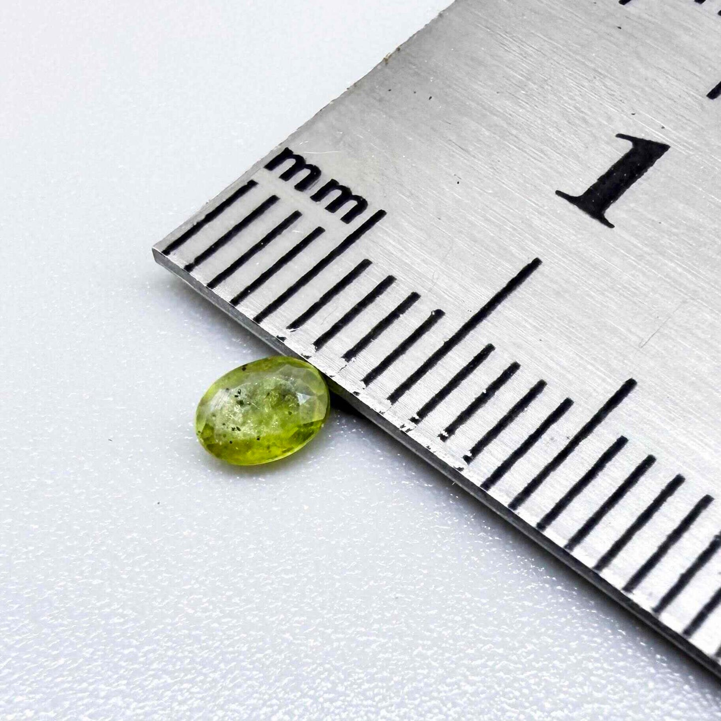 Oval yellow-green sapphire from Thailand, 0.21ct, unheated, with bright greenish-yellow color, visible dark natural inclusions and a transparent to slightly silky appearance.