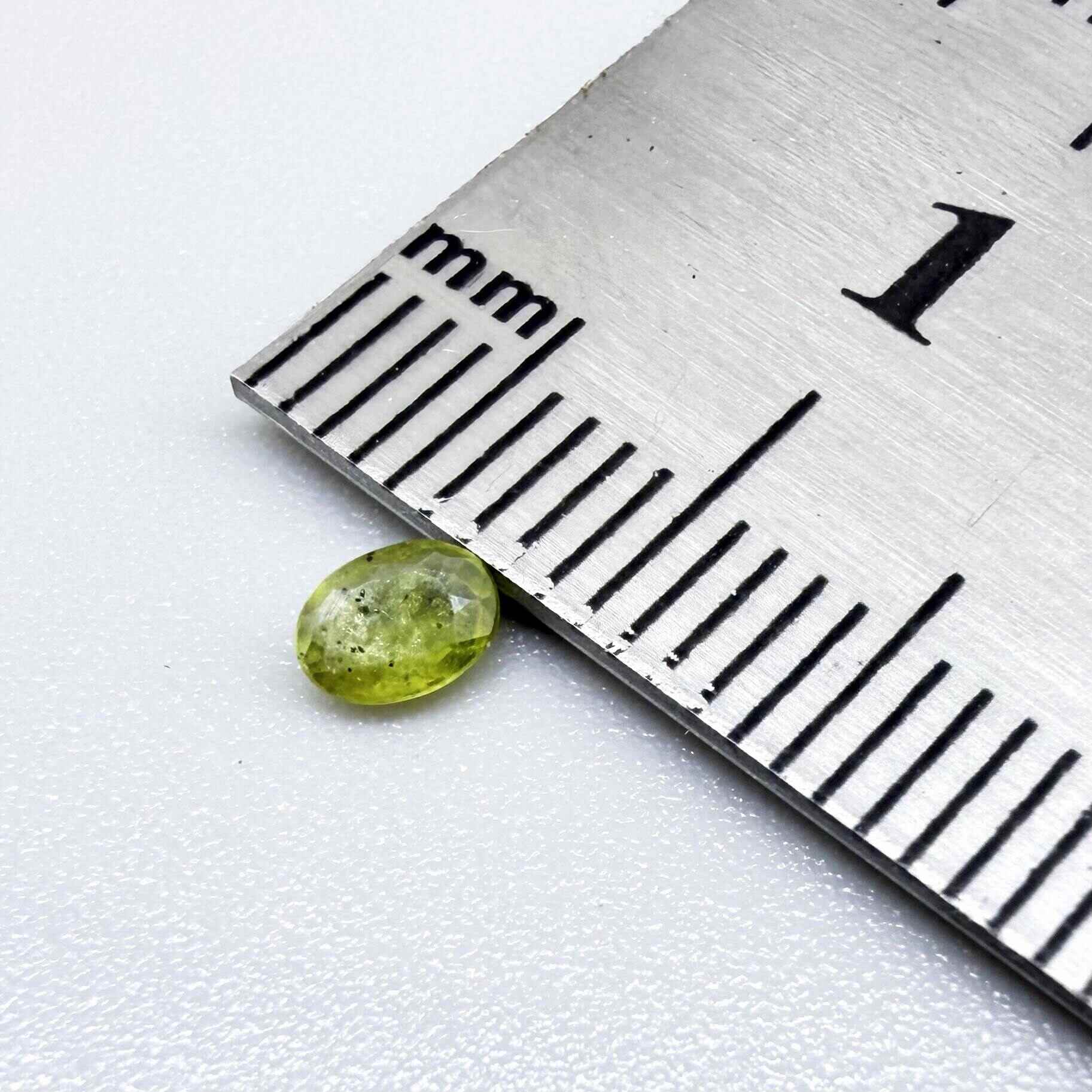 Oval yellow-green sapphire from Thailand, 0.21ct, unheated, with bright greenish-yellow color, visible dark natural inclusions and a transparent to slightly silky appearance.