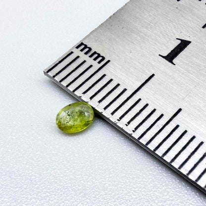 Oval yellow-green sapphire from Thailand, 0.21ct, unheated, with bright greenish-yellow color, visible dark natural inclusions and a transparent to slightly silky appearance.