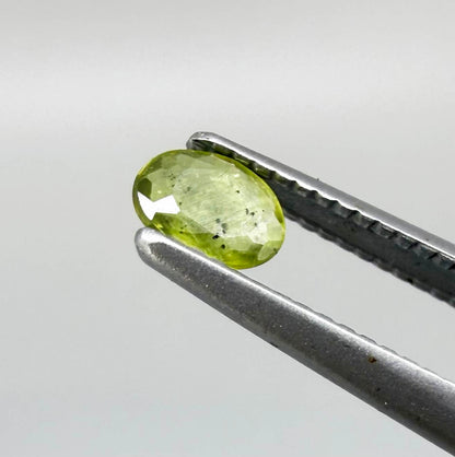 Oval yellow-green sapphire from Thailand, 0.21ct, unheated, with bright greenish-yellow color, visible dark natural inclusions and a transparent to slightly silky appearance.
