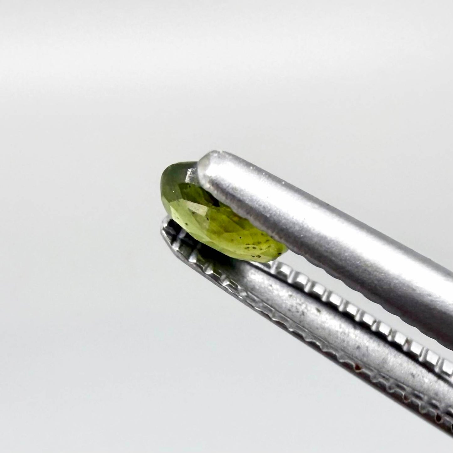 Oval yellow-green sapphire from Thailand, 0.21ct, unheated, with bright greenish-yellow color, visible dark natural inclusions and a transparent to slightly silky appearance.
