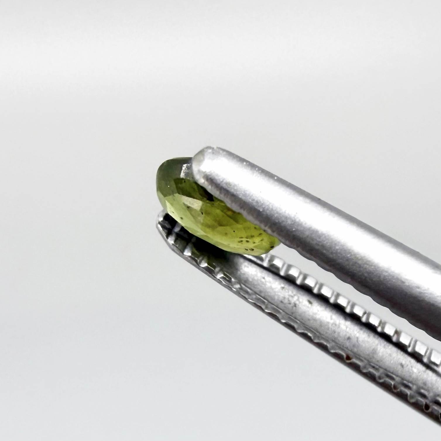 Oval yellow-green sapphire from Thailand, 0.21ct, unheated, with bright greenish-yellow color, visible dark natural inclusions and a transparent to slightly silky appearance.