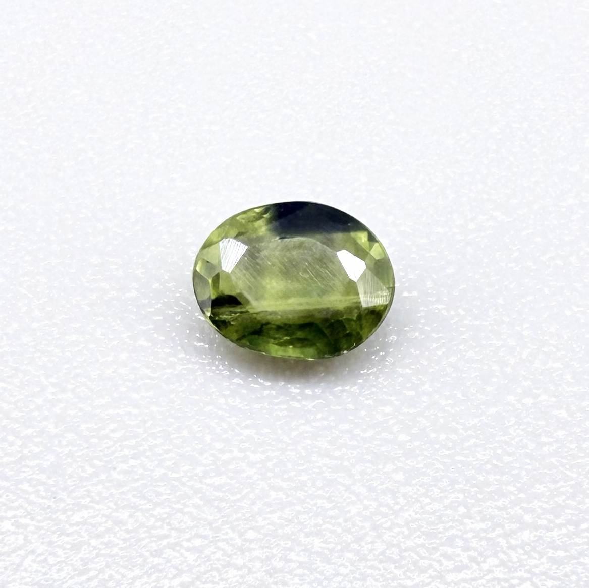 Oval green sapphire from Thailand, 0.37ct, unheated, with olive to deep green color zoning, visible natural inclusions and a transparent to slightly silky appearance.