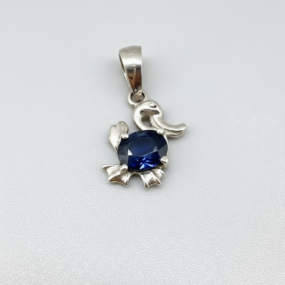 White-gold-plated silver pendant shaped like a duck with a natural sapphire body.