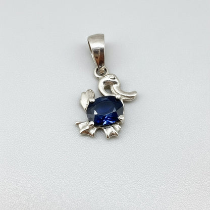 White-gold-plated silver pendant shaped like a duck with a natural sapphire body.