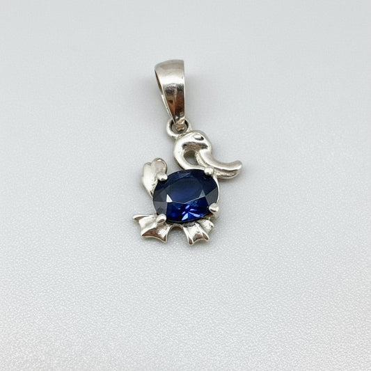 White-gold-plated silver pendant shaped like a duck with a natural sapphire body.