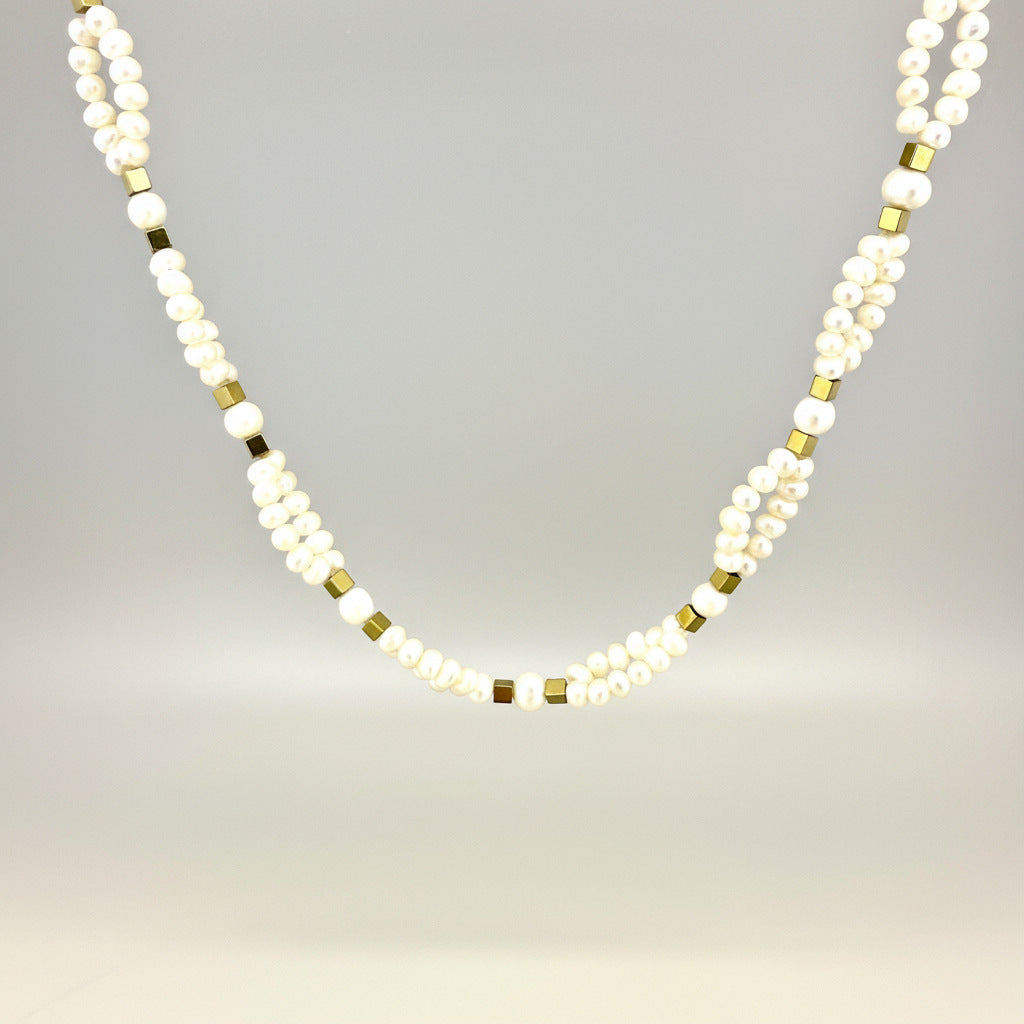 Necklace with alternating white pearls and gold beads on a light gray background