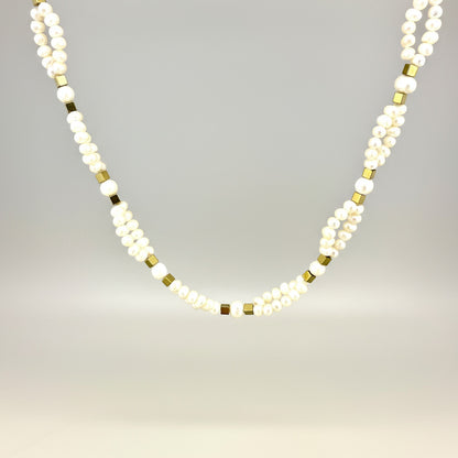 Necklace with alternating white pearls and gold beads on a light gray background