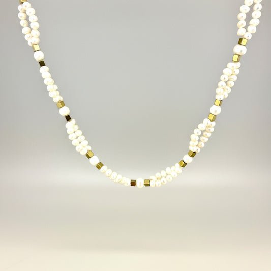 Necklace with alternating white pearls and gold beads on a light gray background