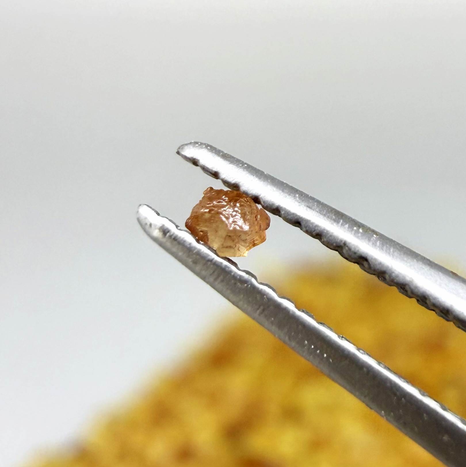 Natural sapphire rough with warm yellow-orange hues and subtle color variation, uncut corundum photographed on neutral background.