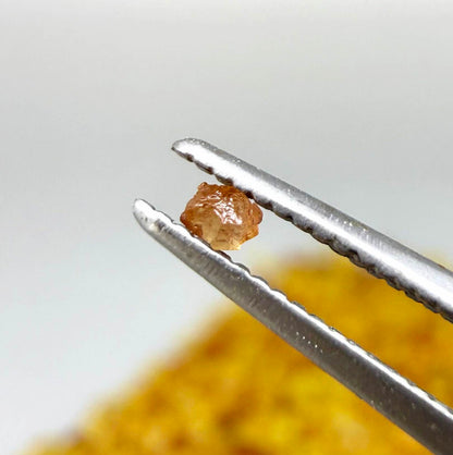 Natural sapphire rough with warm yellow-orange hues and subtle color variation, uncut corundum photographed on neutral background.