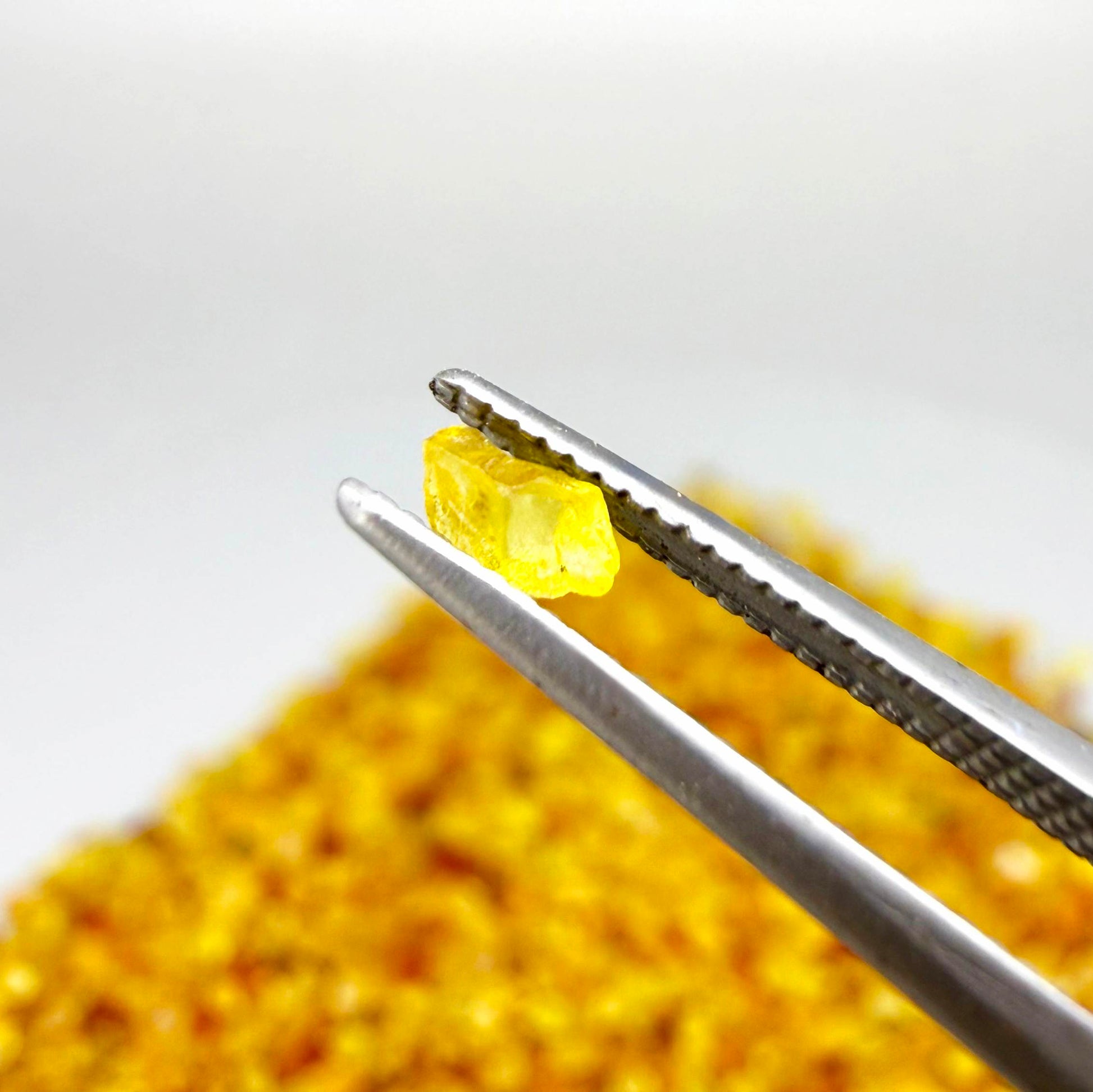 Natural sapphire rough with warm yellow-orange hues and subtle color variation, uncut corundum photographed on neutral background.