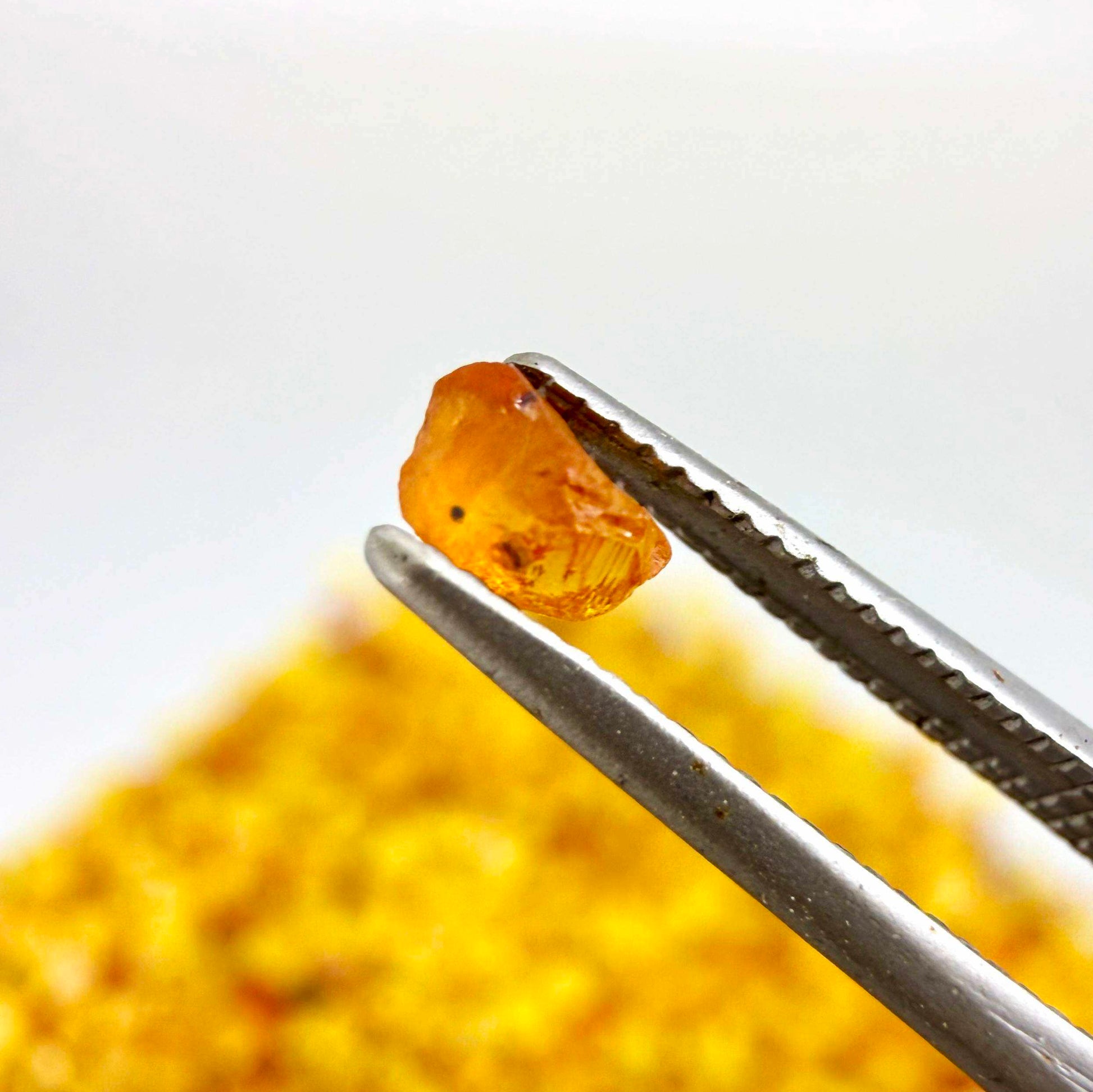 Natural sapphire rough with warm yellow-orange hues and subtle color variation, uncut corundum photographed on neutral background.