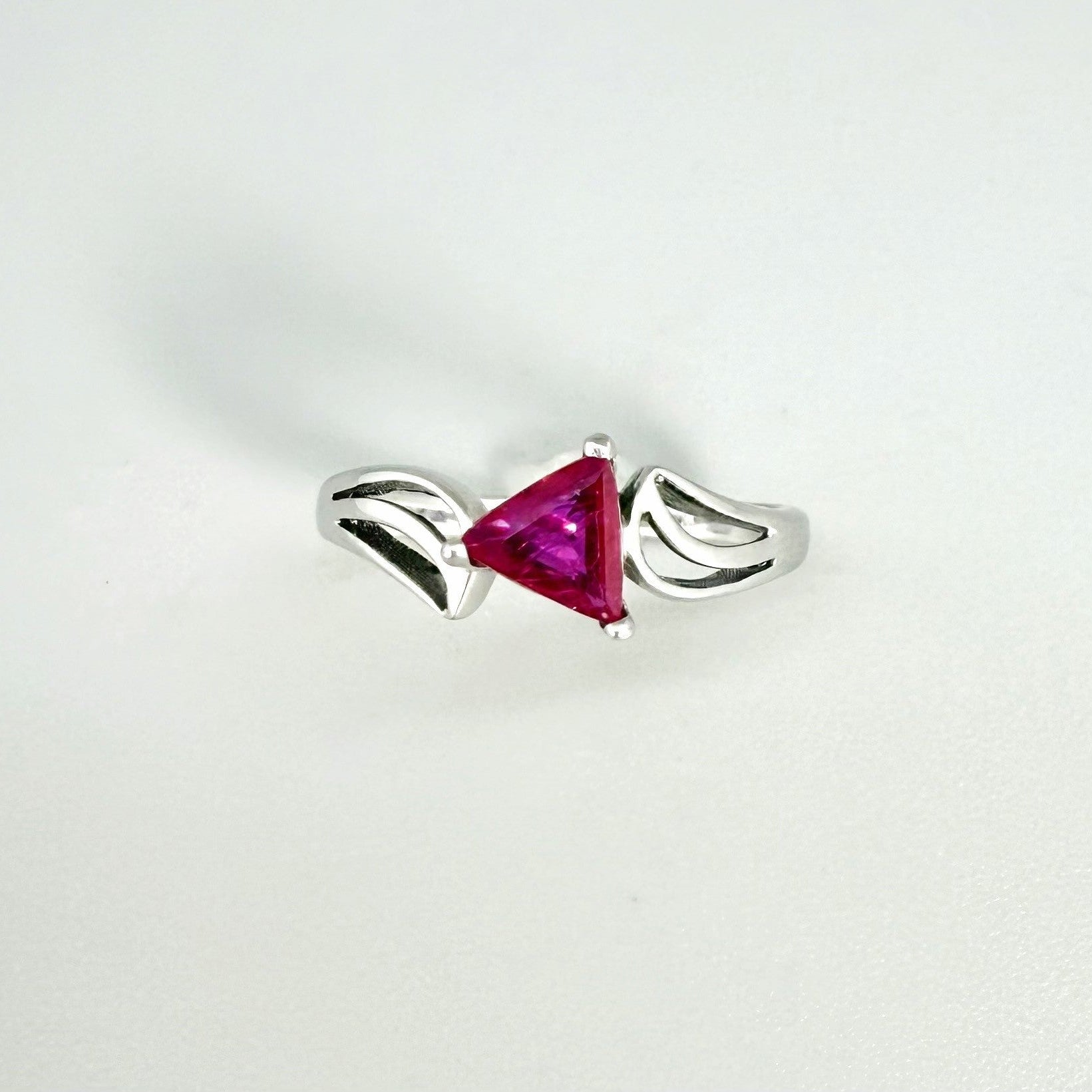 Ruby triangle-cut ring in white gold plated sterling silver, featuring a vivid red natural gemstone in a modern geometric solitaire design.