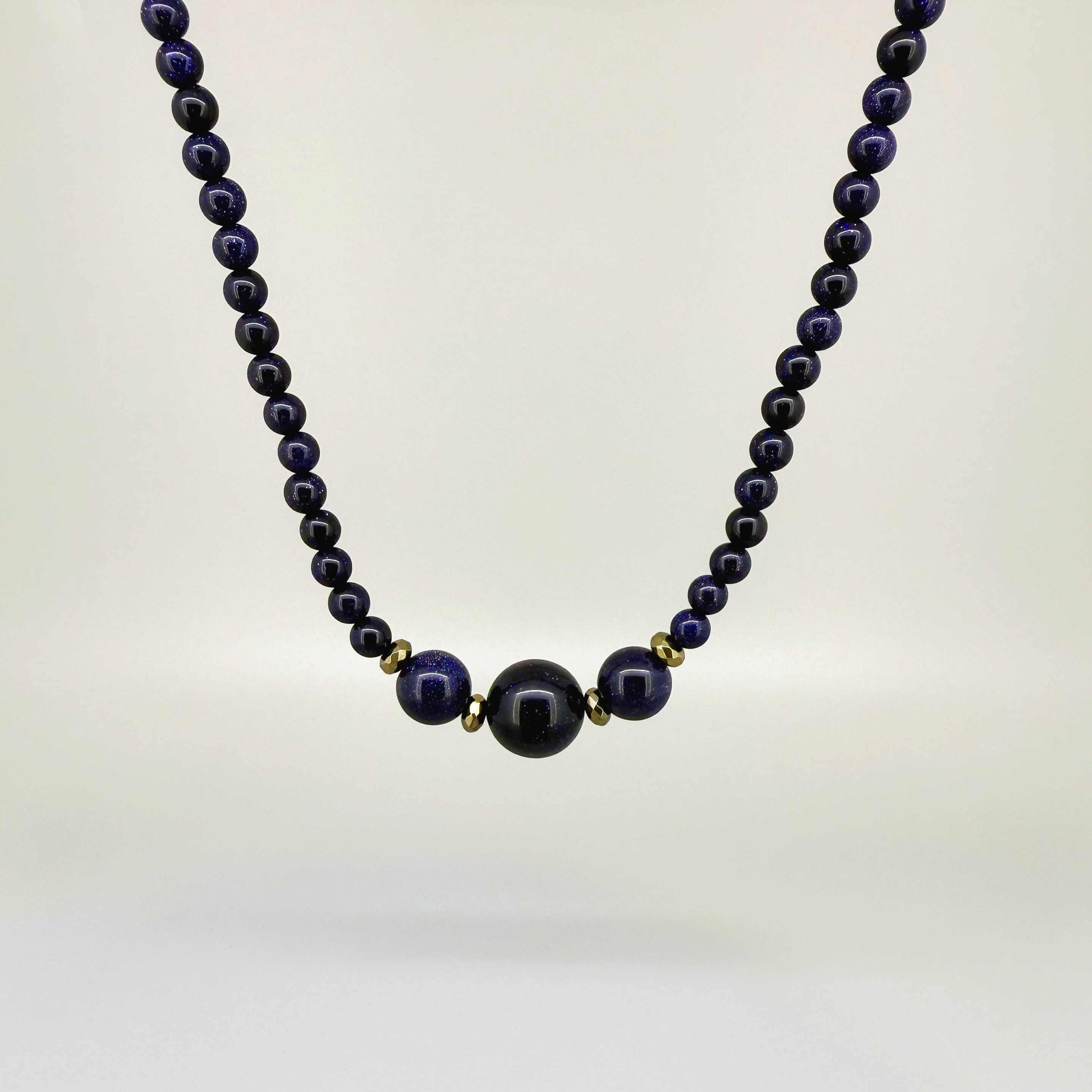 Necklace with dark blue goldstone beads on a light gray background