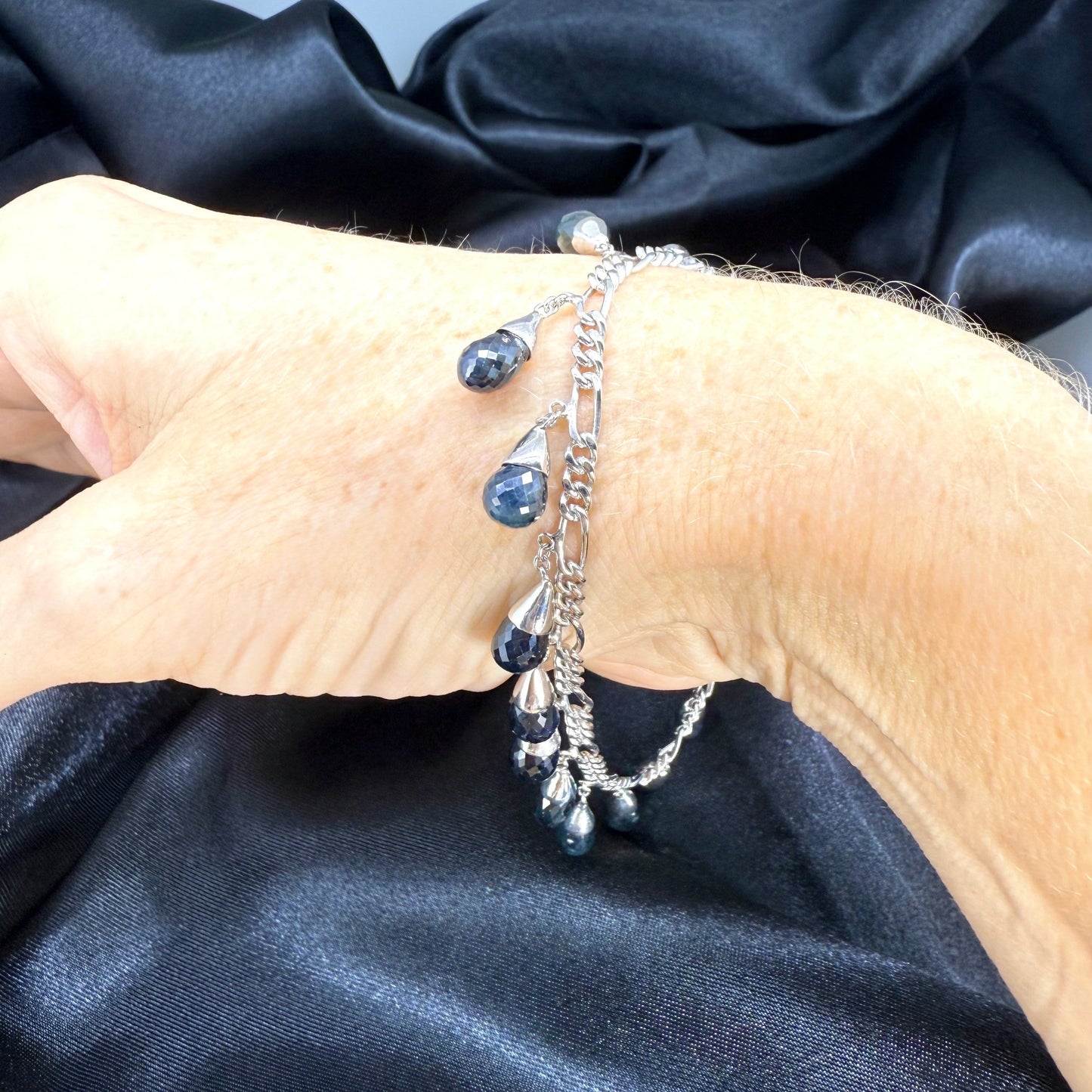Necklace, bracelet and earrings set in white gold plated sterling silver with dark blue pineapple-cut sapphires, elegant jewelry displayed on neutral background.