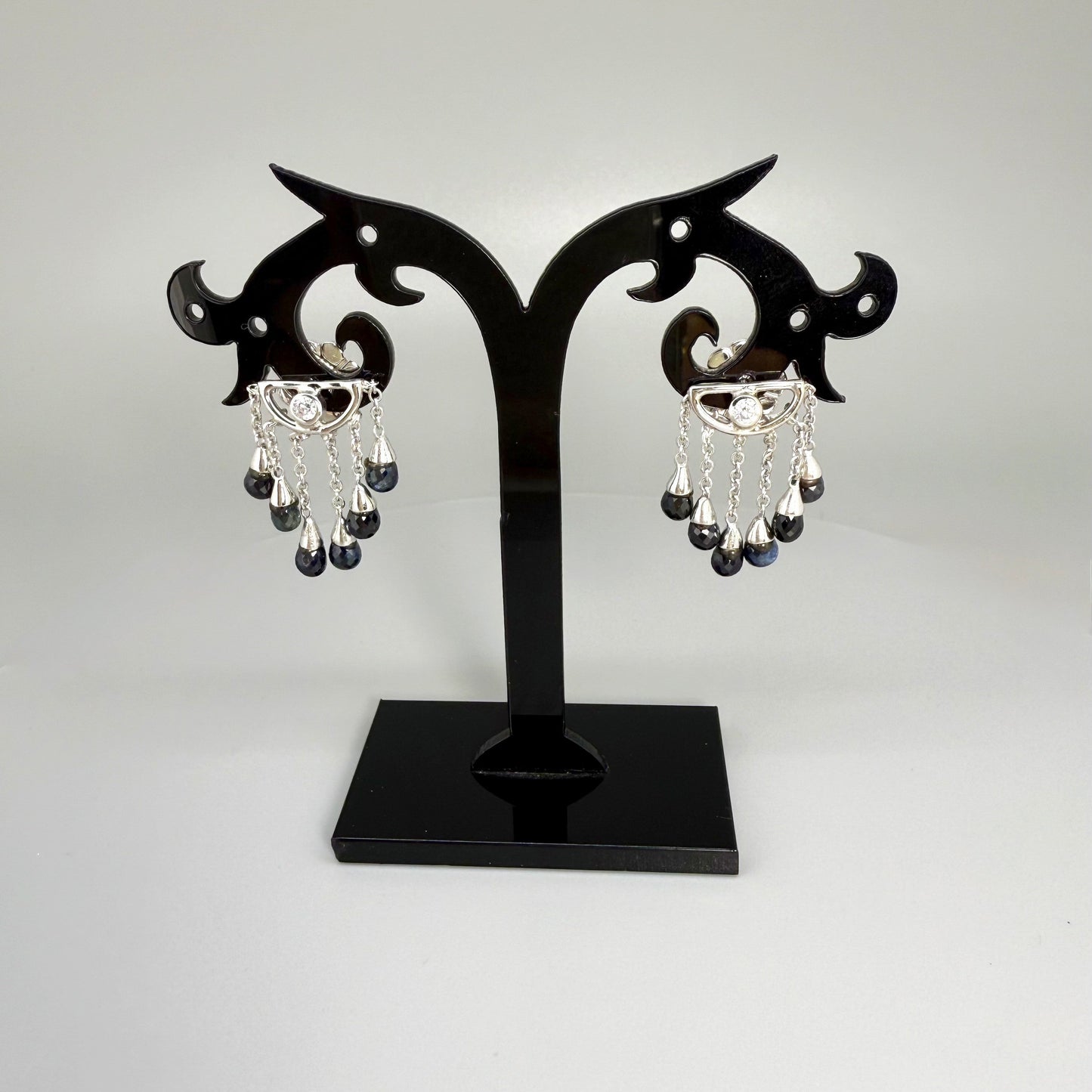 Necklace, bracelet and earrings set in white gold plated sterling silver with dark blue pineapple-cut sapphires, elegant jewelry displayed on neutral background.