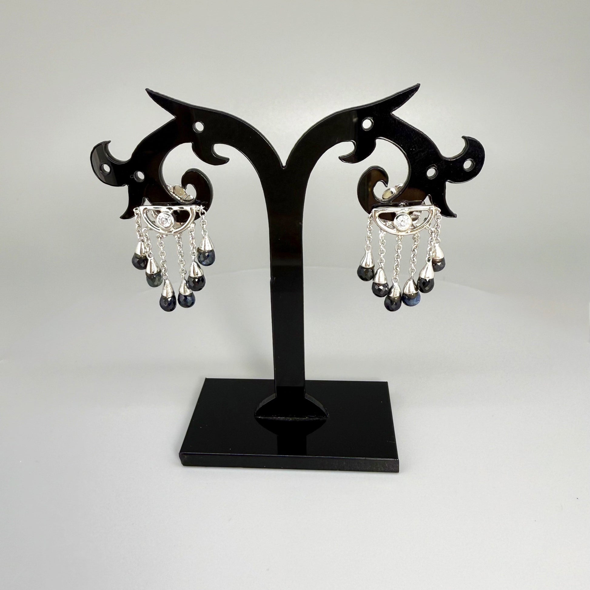 Necklace, bracelet and earrings set in white gold plated sterling silver with dark blue pineapple-cut sapphires, elegant jewelry displayed on neutral background.