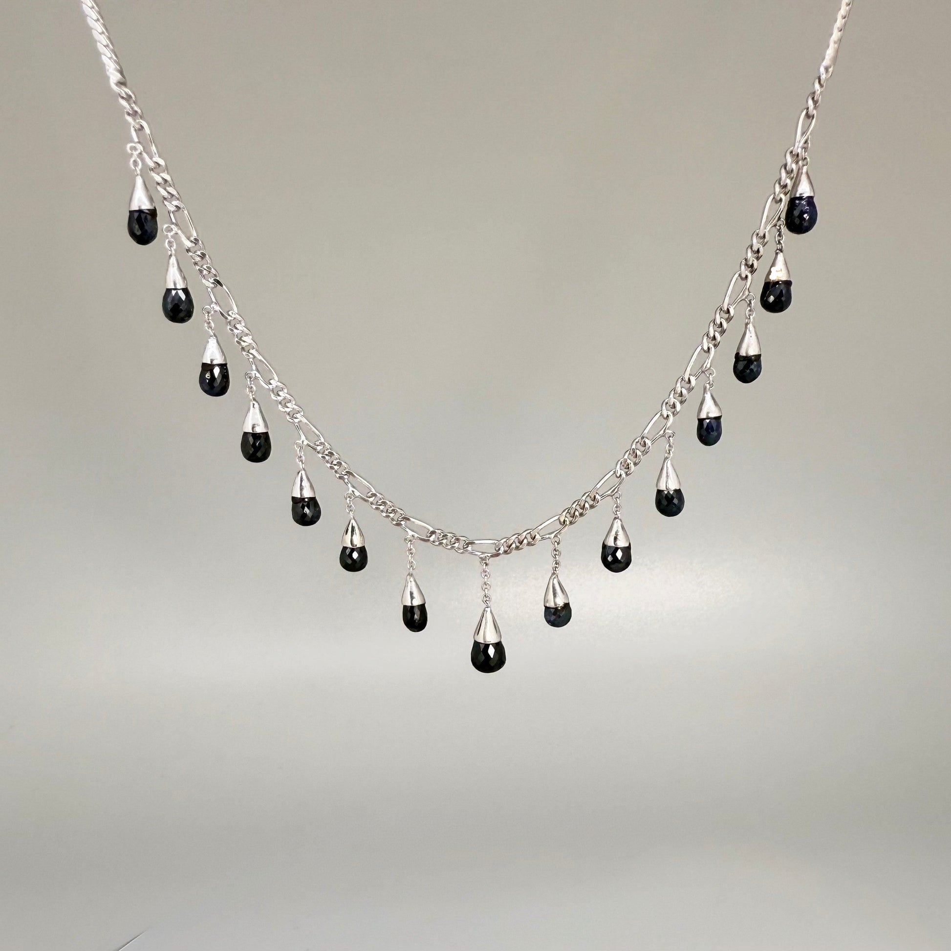 Necklace, bracelet and earrings set in white gold plated sterling silver with dark blue pineapple-cut sapphires, elegant jewelry displayed on neutral background.