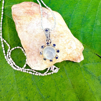 Handcrafted pendant featuring 3.75 ct natural moonstone and 0.35 ct blue sapphires set in white-gold-plated sterling silver.