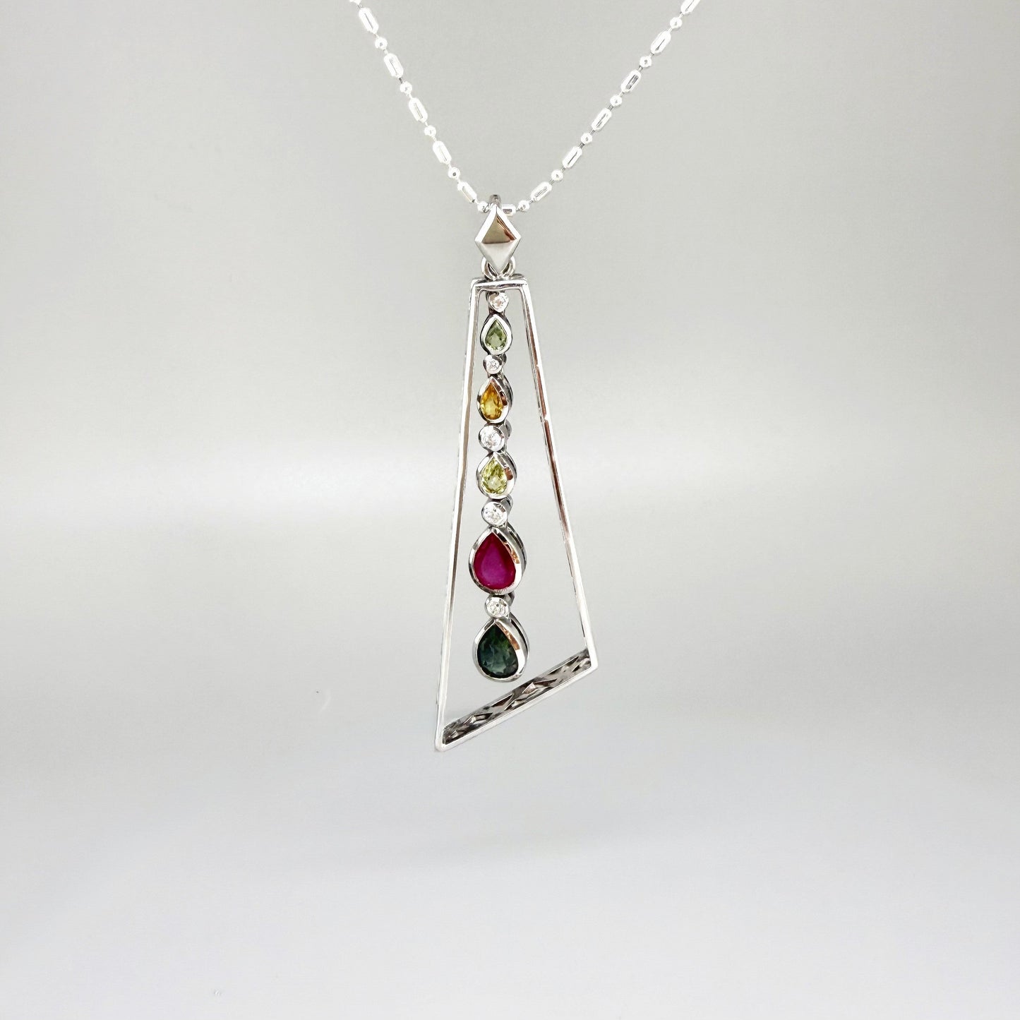 Handmade white gold plated silver pendant featuring 1.97 ct sapphires and 1.32 ct rubies in a modern geometric design with a freely moving gemstone strand.