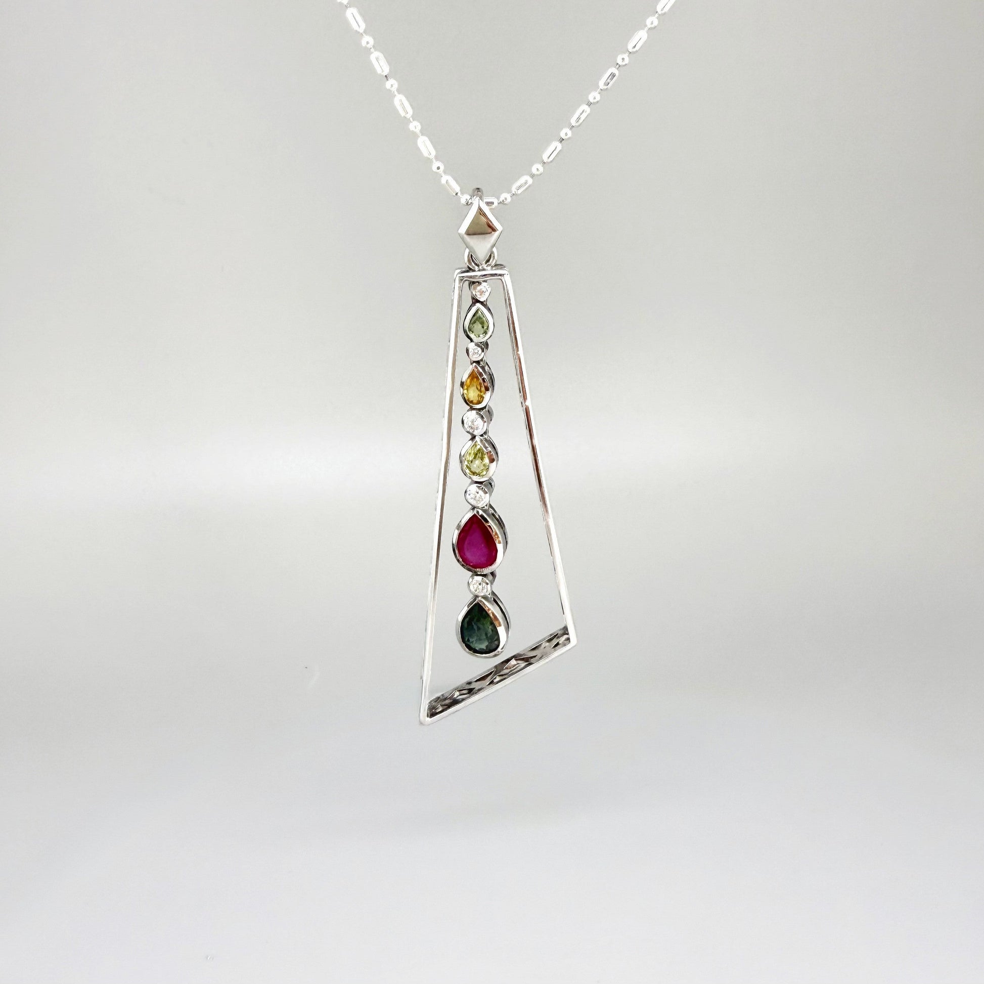 Handmade white gold plated silver pendant featuring 1.97 ct sapphires and 1.32 ct rubies in a modern geometric design with a freely moving gemstone strand.