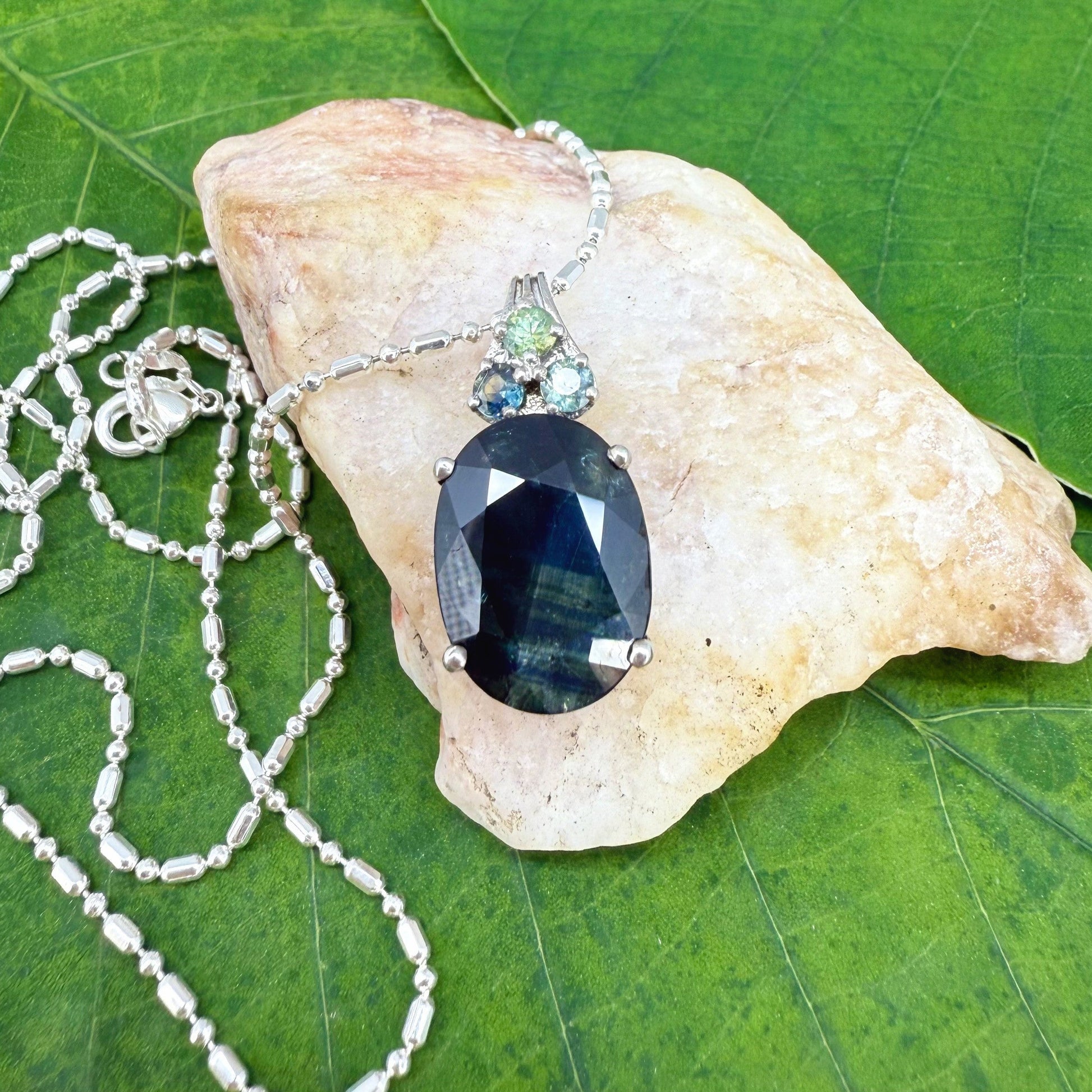 Elegant white gold plated silver pendant with 12.87 ct natural sapphires — one large central gem and three smaller accent stones.