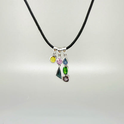 Handcrafted three-pendant gemstone necklace with sapphires, ruby, spinel, and tsavorite (5.81 ct total) on a black leather cord — modular design in white-gold-plated silver.
